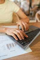 Hands typing on a laptop with business charts on a table, showcasing a productive work environment. photo