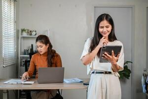 Two women in a modern office setting, one using a laptop and the other a tablet, engaged in work and collaboration. photo