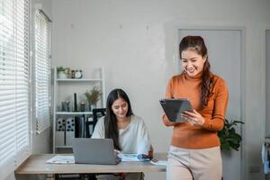 Two women working together in a bright office, using laptops and tablets for a collaborative project. photo