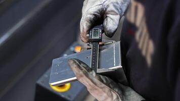 Worker using caliper to measure metal bracket edge with gloves, Precision metalworking inspection in industrial environment video