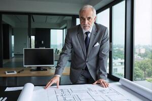 A man in a suit and tie is standing in front of a blueprint photo