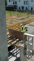 Aerial View of Construction Workers at Building Site. Aerial view captures two construction workers in high-visibility vests as they maneuver a large wooden video