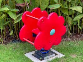 A beautiful red flowershaped playground equipment rocking horse is sitting quietly in the lush green grass at the public park, adding charm to the garden environment photo