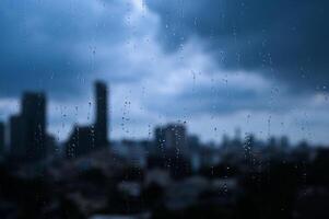 Raindrops on a window with a blurry city skyline in the background under a cloudy sky. photo