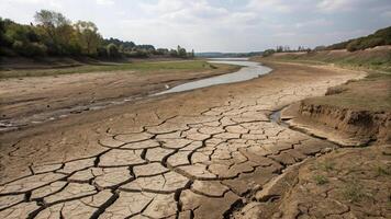 Dried up riverbed with cracked earth, showcasing effects of drought and climate change. landscape features narrow waterway surrounded by parched land and sparse vegetation photo