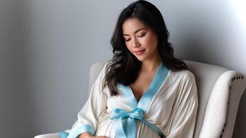 A serene moment captures a pregnant woman in a cream robe with a light blue sash, seated comfortably and embracing her journey into motherhood. photo
