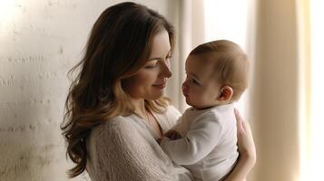 A mother is gently cradling her baby close while both share a tender look, creating a peaceful moment in a bright, serene setting with soft lighting. photo