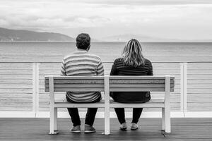 A couple sitting on a bench looking out at the ocean photo