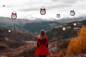 A woman in a red dress standing in front of a mountain with clocks hanging from the sky photo