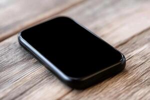 A black smartphone sitting on top of a wooden table photo