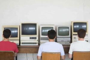 Three men sit at a table with three computers photo