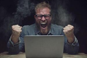 A man with glasses and a beard is sitting in front of a laptop photo
