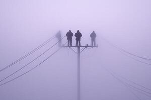 Three people stand on top of a telephone pole in the fog photo