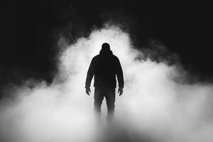 Man in black hoodie standing in fog on black background photo