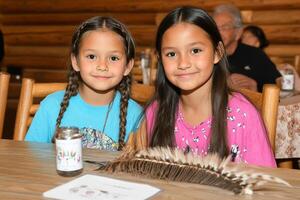 Two young girls pose for a photo at a table with feathers