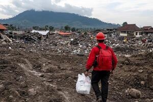 A man in a red shirt and red backpack walking through a dirt road photo