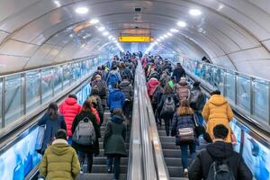 Many people walking down an escalator in an underground tunnel photo
