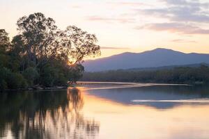 The sun sets over a river with trees and mountains in the background photo