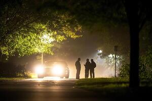 Two people stand on a street at night with a car in the background photo