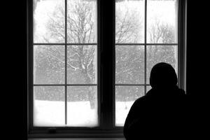 A person is standing in front of a window looking out at snow photo