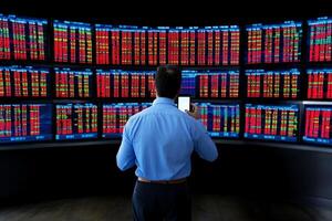 A man standing in front of a large screen with many stock market data photo