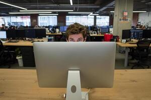 A man is looking at a computer screen in an office photo