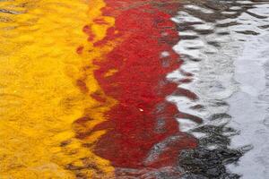A red, yellow and black umbrella is reflected in a puddle photo