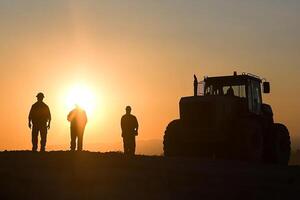 Three men stand in front of a tractor at sunset photo