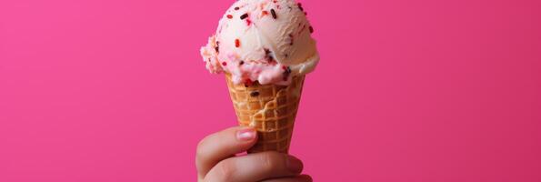 Hand-held ice cream cone with sprinkles on pink background. Banner photo