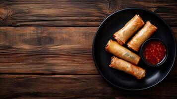Delicious spring rolls with sweet chili sauce served on a modern black plate on a rustic wooden table photo