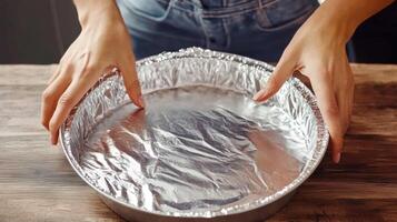 Woman preparing a cake, covered with aluminum foil, in a kitchen setting, showcasing the baking process with a focus on hands in action photo
