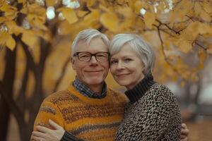 Elderly couple embraces warmly in cozy sweaters beneath autumn trees in soft evening light photo