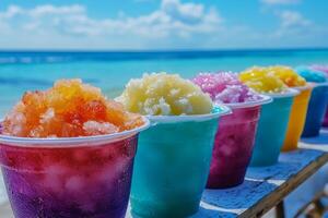 Colorful cups of shaved ice lined up on a table at the beach with a clear ocean backdrop photo