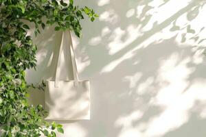 Minimalist canvas tote bag hanging near lush green plants illuminated by soft natural light in a serene indoor setting photo