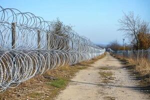 Barbed wire steel wall standing against immigration along a secluded path in Europe during daylight photo