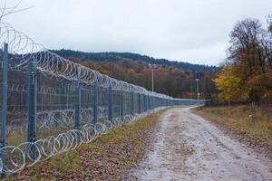 Barbed wire fence along a rural path highlights the challenges of immigration in Europe during uncertain times photo
