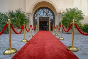 A luxurious red carpet entrance adorned with golden stanchions leading to an elegant venue surrounded by lush greenery photo