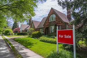 Bright red For Sale sign in front of charming suburban home with lush greenery on a sunny day photo
