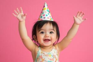 Happy baby girl celebrating in a romper with a party hat against a bright pink background photo