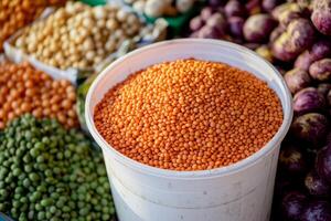 Red lentils in a white bucket at a bustling market surrounded by various legumes and produce photo