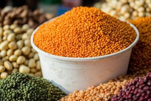 Vibrant red lentils fill a white bucket at a bustling market surrounded by various legumes photo