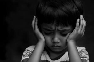 Sad child covering his ears in distress, expressing emotions in a dark environment photo