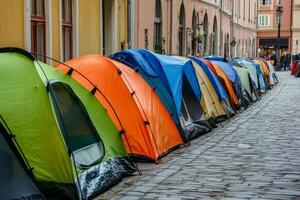Homeless encampment on city street featuring a row of colorful tents lined along the cobblestone pathway near urban buildings photo