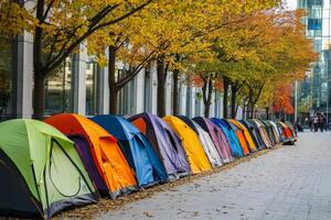 Brightly colored tents create a homeless encampment along a city street lined with autumn trees photo