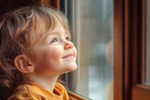 A child gazes happily out of a window, enjoying the view on a rainy day in a cozy room filled with warmth and light photo