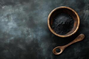 Activated charcoal powder in a wooden bowl with a spoon against a black background for natural wellness and beauty applications photo