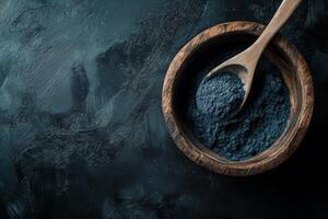 Activated charcoal powder displayed in a wooden bowl with a spoon against a black textured background photo
