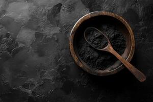 Activated charcoal powder in a wooden bowl with a spoon on a textured black background showcasing natural beauty and health benefits photo