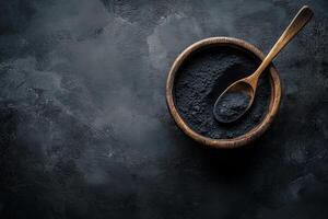Activated charcoal powder in a wooden bowl with a spoon on a black background for natural remedies and beauty treatments photo