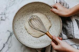Close-up of hands whisking dough in a speckled bowl on a kitchen countertop for baking and cooking enthusiasts photo